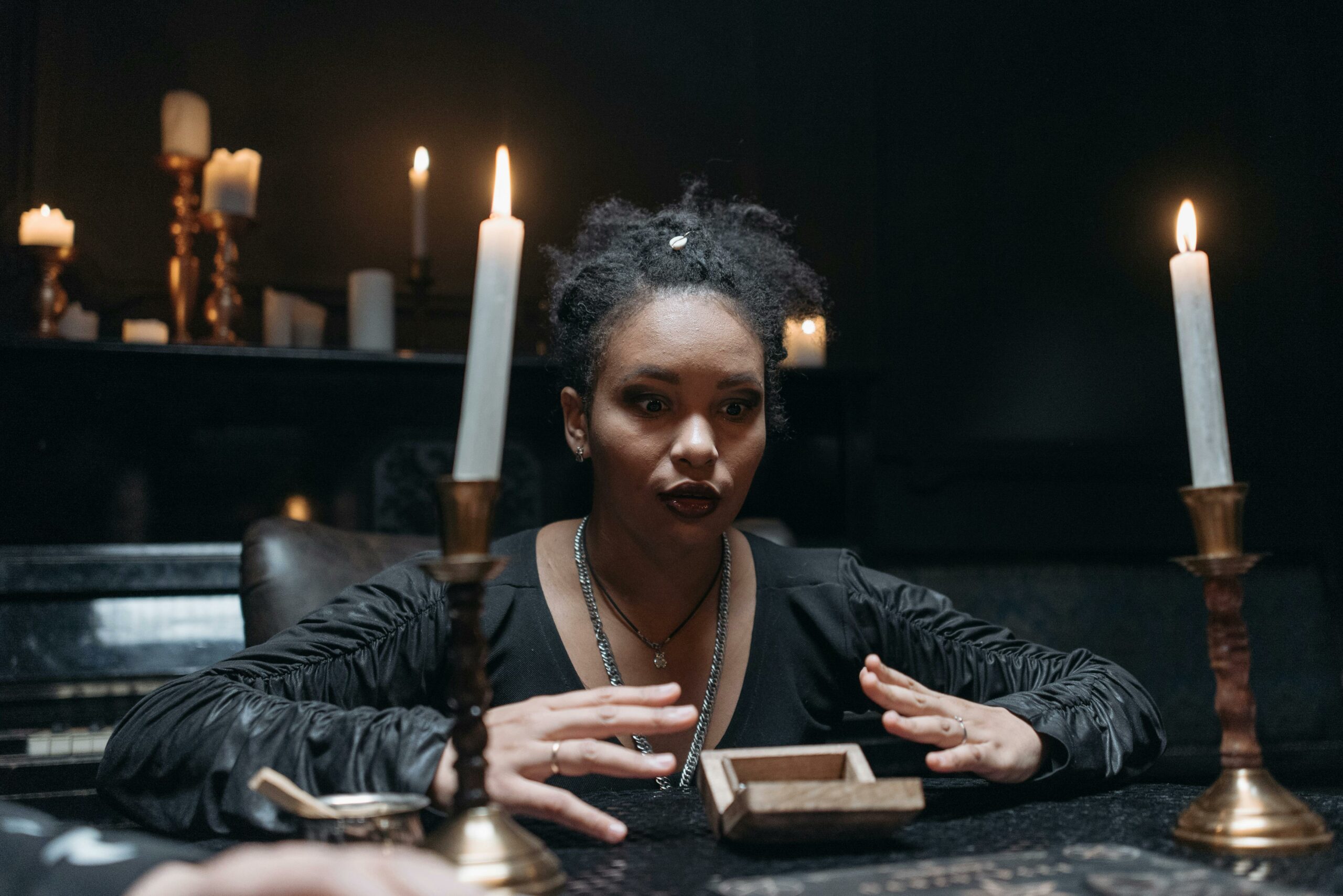 A medium surrounded by candles in a dark, mysterious setting, engaging in a seance.